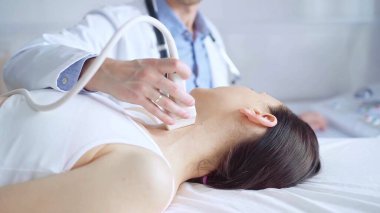 Doktor adam, muayene için kadın hastanın boynuna ultrason cihazı takıyor. Tıp ve Bilim.