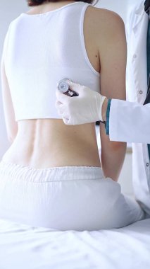 Doktor ve hasta. Tıbbi eldiven giyen doktor, klinikte arka taraftan kadın ciğerlerini incelemek için steteskop kullanıyor. İlaç ve sağlık hizmetleri.