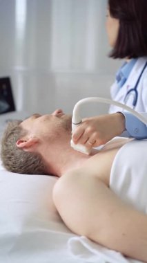 Doktor, muayene masasında yatan erkek hastanın boynunu incelemek için ultrason cihazı kullanıyor.