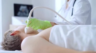 Yeşil eldivenli doktor kadın erkek hastaya boyun ultrasonu yapıyor. Tiroid bezi muayenesi. Tıp konsepti.
