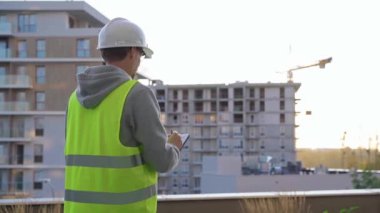 İnşaat mühendisi kadın. Gün batımında inşaat alanını incelerken not alıyor ve panoya yazı yazıyor..