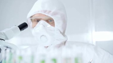 Koruyucu ekipman kullanan profesyonel bilim adamı laboratuvar ortamında mikroskop kullanıyor. Bilim ve tıp.