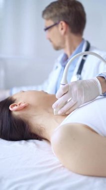 Beyaz koruyucu eldiven giyen doktor hasta kadının boynuna ultrason cihazı takıyor ve muayene için yalan söylüyor. Tıp konsepti.