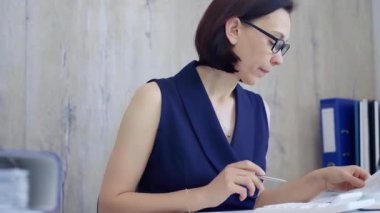 İş kadını ofisteki masasında kağıt işleriyle uğraşıyor, hesap makinesi kullanıyor ve not alıyor. Vergiler, iş denetimleri.