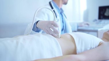 Doktor, iç organlarını inceleyen bir kadın hastaya ultrason cihazı kullanarak mavi eldiven takıyor. Tıpta önleyici terapi.