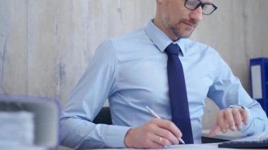 Masrafları hesaplarken ve masasında notlar alırken mavi tişörtlü bir erkek muhasebeci. Vergiler, iş denetimleri.