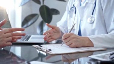 Doktor ve hasta sağlık sorunlarını muayenehanede tartışıyorlar. Doktor bir not panosuna not alıyor. İlaç ve Sağlık Hizmetleri.