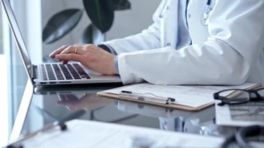 Doktor, klinikteki cam bir masada hasta kayıtları için dizüstü bilgisayar kullanıyor. Tıp konsepti.