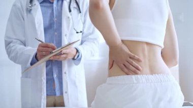 Doktor adam, hasta kadın sırt ağrısından bahsederken bir not panosuna not alıyor. Tıp ve ortopedi kavramları.