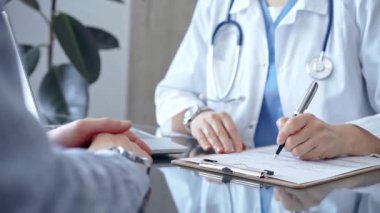 Doktor ve hasta sağlık sorunlarını muayenehanede tartışıyorlar. Doktor bir not panosuna not alıyor. İlaç ve Sağlık Hizmetleri.