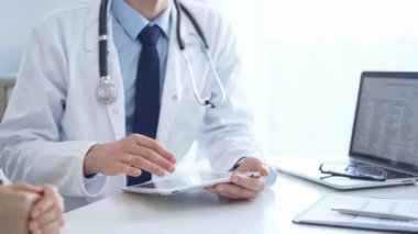 Doktor ve bir hasta. Mavi gömleğin üzerine beyaz bir tıbbi önlük giyen hekim klinikteki muayene sırasında tablet bilgisayar kullanıyor. İlaç..