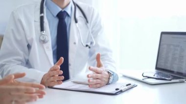 Doktor ve bir hasta. Doktor, mavi gömlek ve kravatın üzerine beyaz bir ceket giyiyordu. Klinikteki muayene sırasında elleriyle el kol hareketi yapıyordu. Tıp konsepti