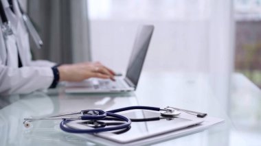 Tablet bilgisayar ve mavi steteskop cam masanın üzerindeyken doktor kadın cam masada dizüstü bilgisayar kullanıyor. Tıp konsepti.