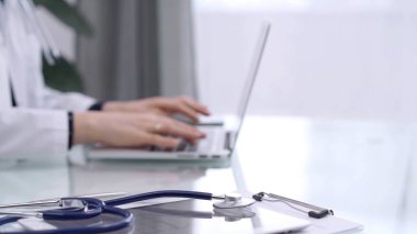 Tablet bilgisayar ve steteskop cam masada yatarken doktor kadın cam masada dizüstü bilgisayar kullanıyor. Tıp konsepti.