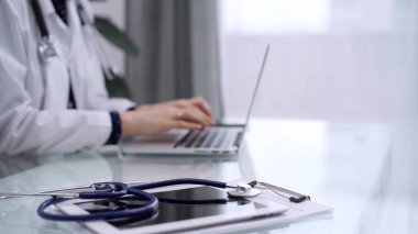 Tablet bilgisayar ve mavi steteskop cam masanın üzerindeyken doktor kadın cam masada dizüstü bilgisayar kullanıyor. Tıp konsepti.