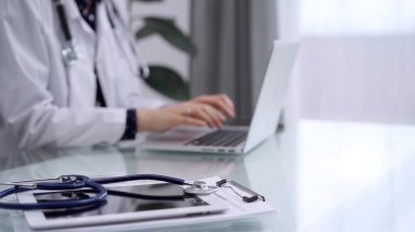 Tablet bilgisayar ve mavi steteskop cam masanın üzerindeyken doktor kadın cam masada dizüstü bilgisayar kullanıyor. Tıp konsepti.