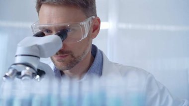 Koruyucu gözlüklü ve eldivenli bilim adamı laboratuvarda mikroskop kullanıyor. Araştırmacı portresi. Mikrobiyoloji bilim konsepti.