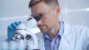 Koruyucu gözlüklü ve eldivenli bilim adamı laboratuvarda mikroskop kullanıyor. Araştırmacı portresi. Mikrobiyoloji bilim konsepti.