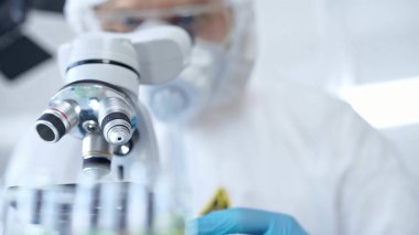 Koruyucu ekipman kullanan profesyonel bilim adamı bir laboratuvar ortamında mikroskop kullanıyor, yakın plan. Bilim ve tıp kavramları.