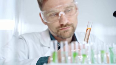 Güvenlik gözlüklü bir araştırmacı modern bir laboratuvarda turuncu bir sıvıyla laboratuvar tüpünü inceliyor. Bilim, mikrobiyoloji ve tıp.