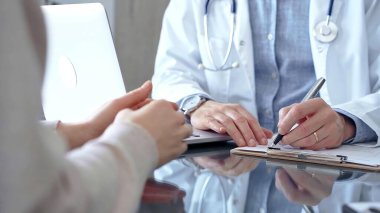 Doktor, elinde bir kalem ve not panosuyla hastaya danışmanlık yaparken notlar alıyor. Tıbba güven kavramı.