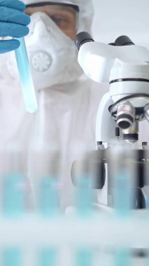 Profesyonel bilim adamı, mikroskobun yanındaki tüp örneğini dikkatlice analiz ediyor.