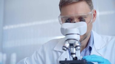 Koruyucu gözlüklü ve eldivenli bilim adamı laboratuvarda mikroskop kullanıyor. Araştırmacı portresi. Mikrobiyoloji bilim konsepti.