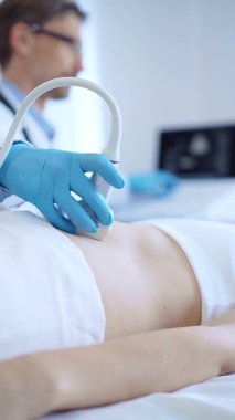 Doktor, iç organlarını inceleyen bir kadın hastaya ultrason cihazı kullanarak mavi koruyucu eldiven takıyor. Tıp konsepti.