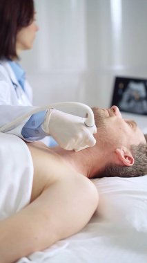 Doktor, muayene masasında yatan erkek hastanın boynunu incelemek için ultrason cihazı kullanıyor.