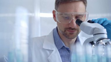 Koruyucu gözlüklü ve eldivenli bilim adamı laboratuvarda mikroskop kullanıyor. Araştırmacı portresi. Mikrobiyoloji bilim konsepti.