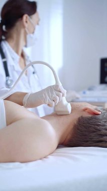 Beyaz tıbbi eldivenli doktor kadın erkek hastaya boyun ultrasonu yapıyor. Tiroid bezi muayenesi. Tıp konsepti.