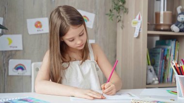 Young girl intently drawing with colored pencils on paper, in a bright, artistic home setting clipart