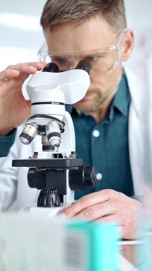 Koruyucu gözlüklü bilim adamı laboratuvarda mikroskop kullanıyor. Mikrobiyoloji bilim konsepti.