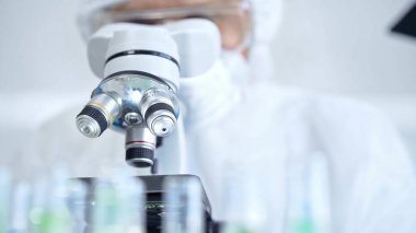 Koruyucu ekipman kullanan profesyonel bilim adamı bir laboratuvar ortamında mikroskop kullanıyor, yakın plan. Bilim ve tıp kavramları.