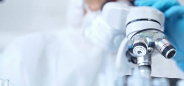 Koruyucu ekipman kullanan profesyonel bilim adamı bir laboratuvar ortamında mikroskop kullanıyor, yakın plan. Bilim ve tıp kavramları.