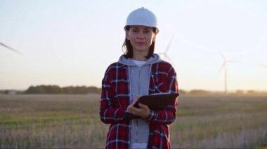 Kadın mühendis, güneş batarken rüzgar türbinleriyle dolu bir alanda dimdik duruyor. Temiz enerji ve mühendislik denetimi kavramı.