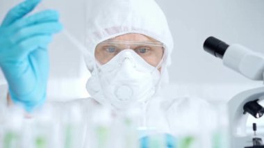 Prezervatif kullanan profesyonel bilim adamı pipetini kullanıyor ve laboratuvar ortamında test tüpünü inceliyor..
