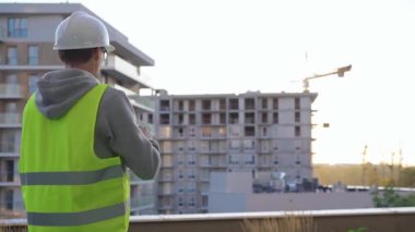 İnşaat erkek mühendisi, sabah güneş doğarken inşaat alanını incelerken tablet bilgisayarla not alıyor..