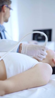 Beyaz koruyucu eldiven giyen doktor hastanedeki kadın hastayı muayene etmek için ultrason makinesi kullanıyor. İlaç, tiroit bezi, sağlık..
