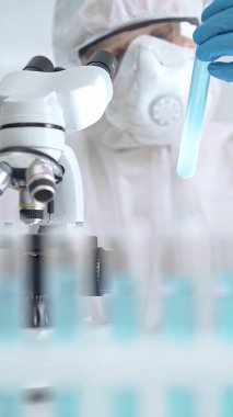 Profesyonel bilim adamı, mikroskobun yanındaki tüp örneğini dikkatlice analiz ediyor.