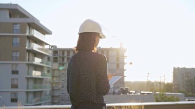 Başlık takan kadın mimar, sabah güneş doğarken inşaat alanını incelerken tablet bilgisayarla not alıyor..