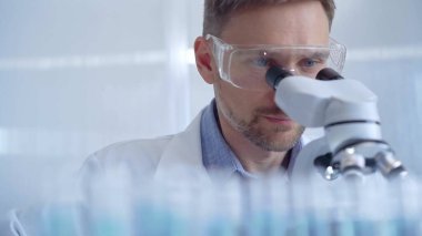 Koruyucu gözlüklü ve eldivenli bilim adamı laboratuvarda mikroskop kullanıyor. Araştırmacı portresi. Mikrobiyoloji bilim konsepti.