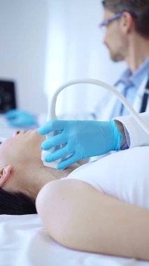 Mavi koruyucu eldiven giyen doktor, klinikteki kadın hastayı muayene etmek için ultrason makinesi kullanıyor. İlaç, tiroit bezi muayenesi..
