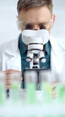 Koruyucu gözlüklü bilim adamı laboratuvarda mikroskop kullanıyor. Mikrobiyoloji bilim konsepti.