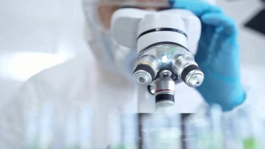 Koruyucu ekipman kullanan profesyonel bilim adamı bir laboratuvar ortamında mikroskop kullanıyor, yakın plan. Bilim ve tıp kavramları.