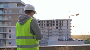 Beyaz miğfer ve güvenlik yeleği takan mühendis, sabahın erken saatlerinde bir inşaat alanını incelerken not alıyor..