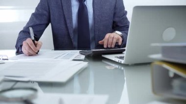 Mavi takım elbiseli bir işadamı profesyonel ofis ortamında dizüstü bilgisayar, hesap makinesi ve belgelerle çalışıyor. Düşük ışıklandırma, yakın görüş. İş adamları, denetim kavramı.