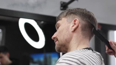 Profesyonel berber, erkek müşterilerin saçlarını makas ve tarakla buduyor. Modern saç stilini modern kuaförde yaratıyor..