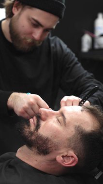 Profesyonel berber müşterilerinin sakallarını ustura ile tıraş eder, jöle sürer ve modern berber ortamında titizlikle bakımı için sıcak havlu kullanır..