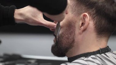 Profesyonel berber, müşterinin sakalını ustura ile dikkatlice tıraş ederek modern bir berber dükkanında kusursuz ve şık bir tımar deneyimi sağlar.